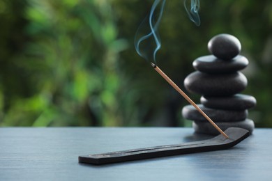 Photo of Incense stick smoldering in holder and spa stones on wooden table outdoors, space for text. Om ligature