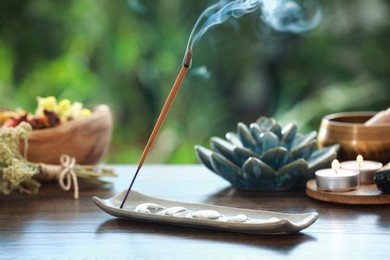 Incense stick smoldering in holder and burning candles on wooden table outdoors