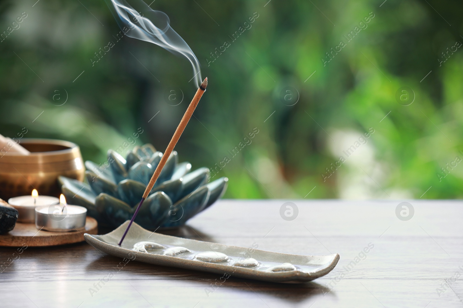 Photo of Incense stick smoldering in holder and burning candles on wooden table outdoors