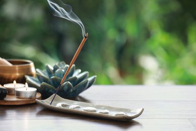 Photo of Incense stick smoldering in holder and burning candles on wooden table outdoors