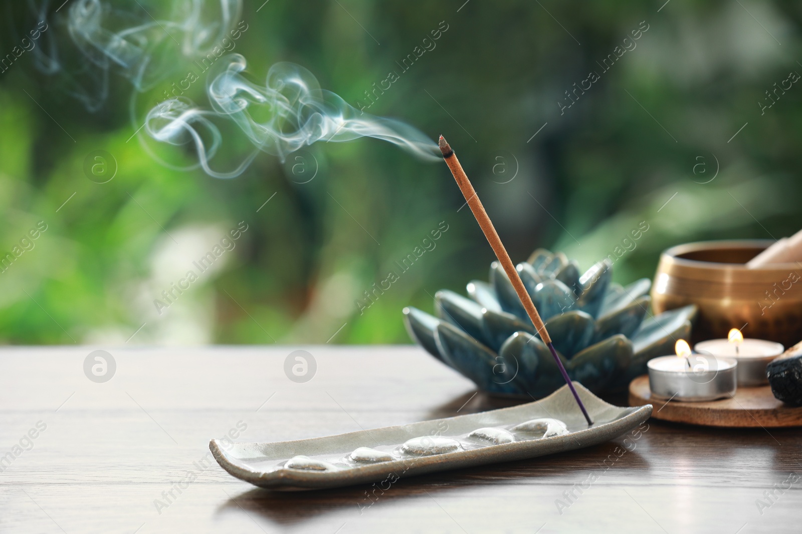 Photo of Incense stick smoldering in holder and burning candles on wooden table outdoors