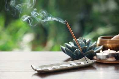 Photo of Incense stick smoldering in holder and burning candles on wooden table outdoors