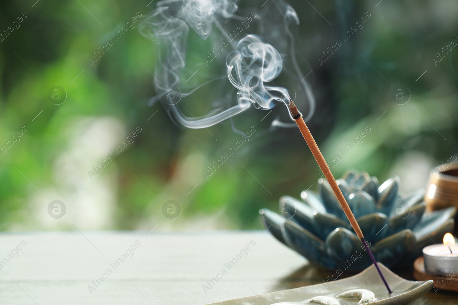 Photo of Incense stick smoldering in holder and burning candle on table outdoors, space for text