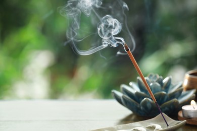 Photo of Incense stick smoldering in holder and burning candle on table outdoors, space for text