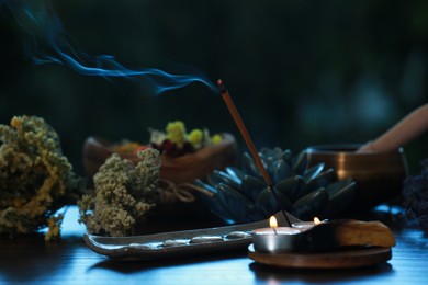 Photo of Incense stick smoldering in holder, candles and dry flowers on wooden table outdoors