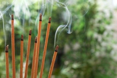 Photo of Incense sticks smoldering on green blurred background, space for text