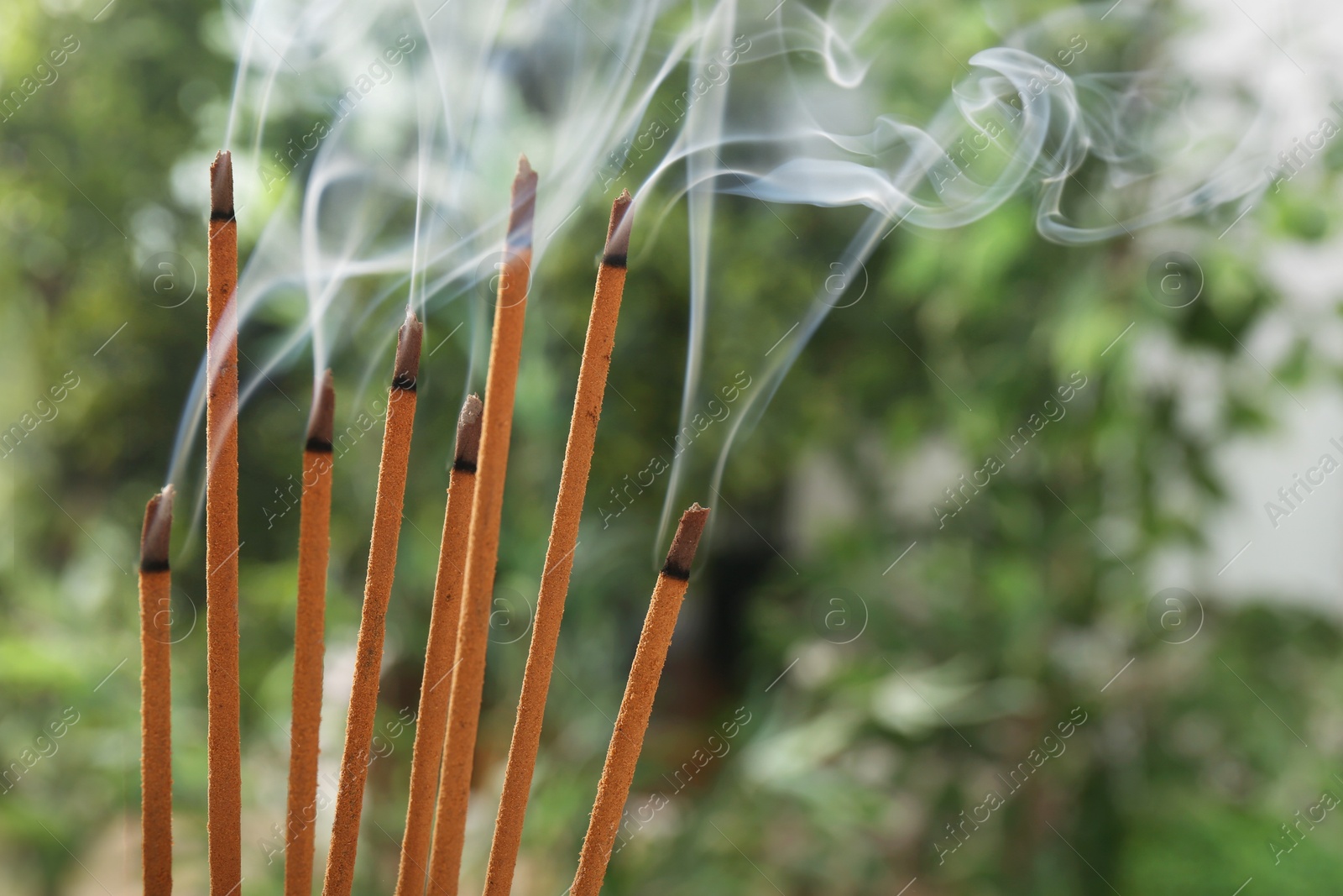 Photo of Incense sticks smoldering on green blurred background, space for text