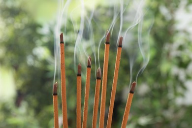 Photo of Incense sticks smoldering on green blurred background