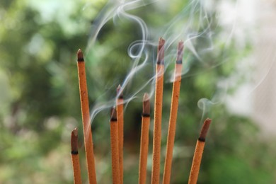 Photo of Incense sticks smoldering on green blurred background