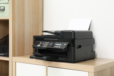 Modern printer with paper on wooden nightstand in office