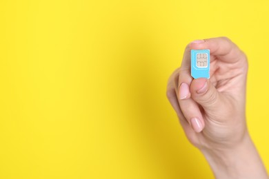 Photo of Woman holding SIM card on yellow background, closeup. Space for text