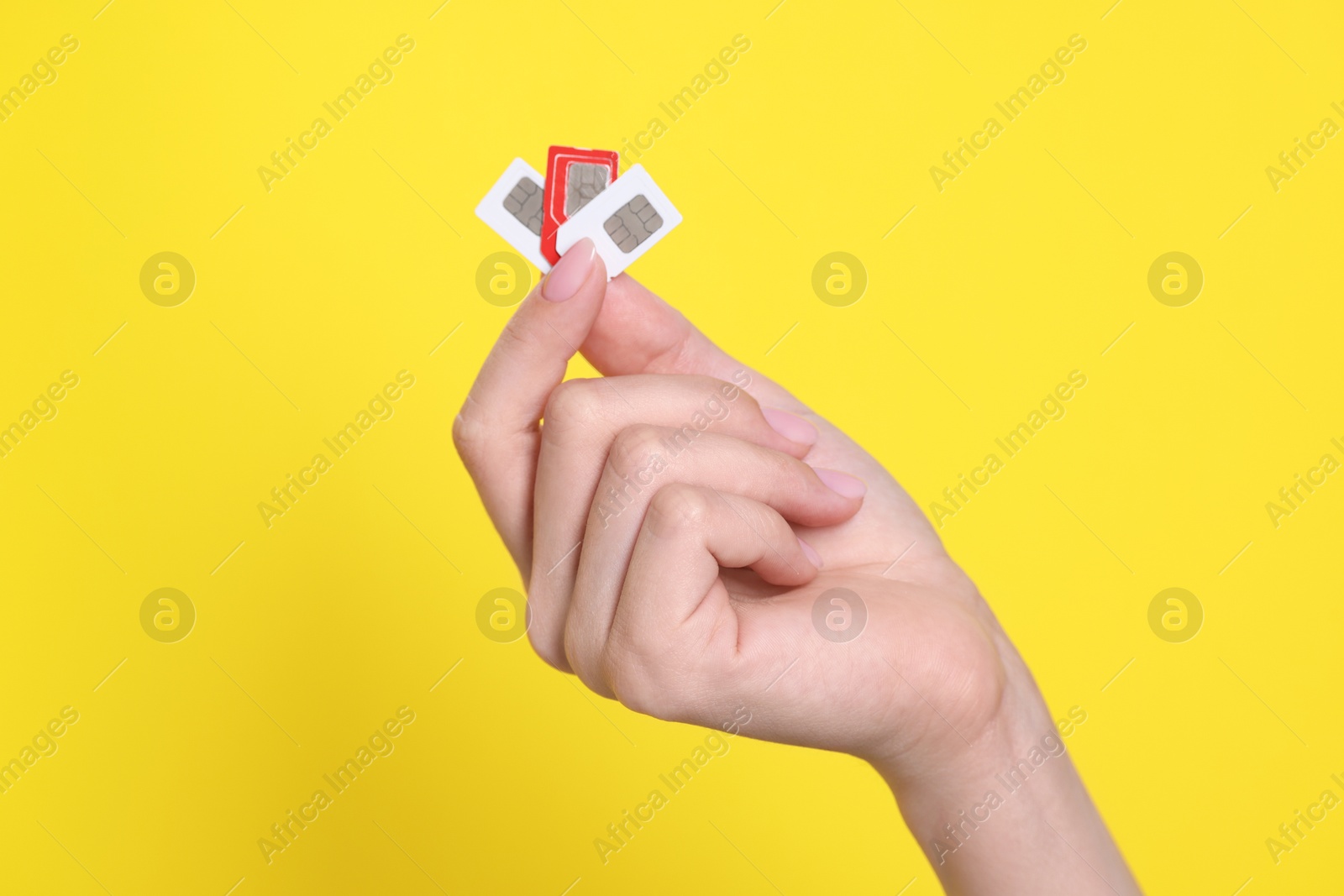 Photo of Woman holding SIM cards on yellow background, closeup