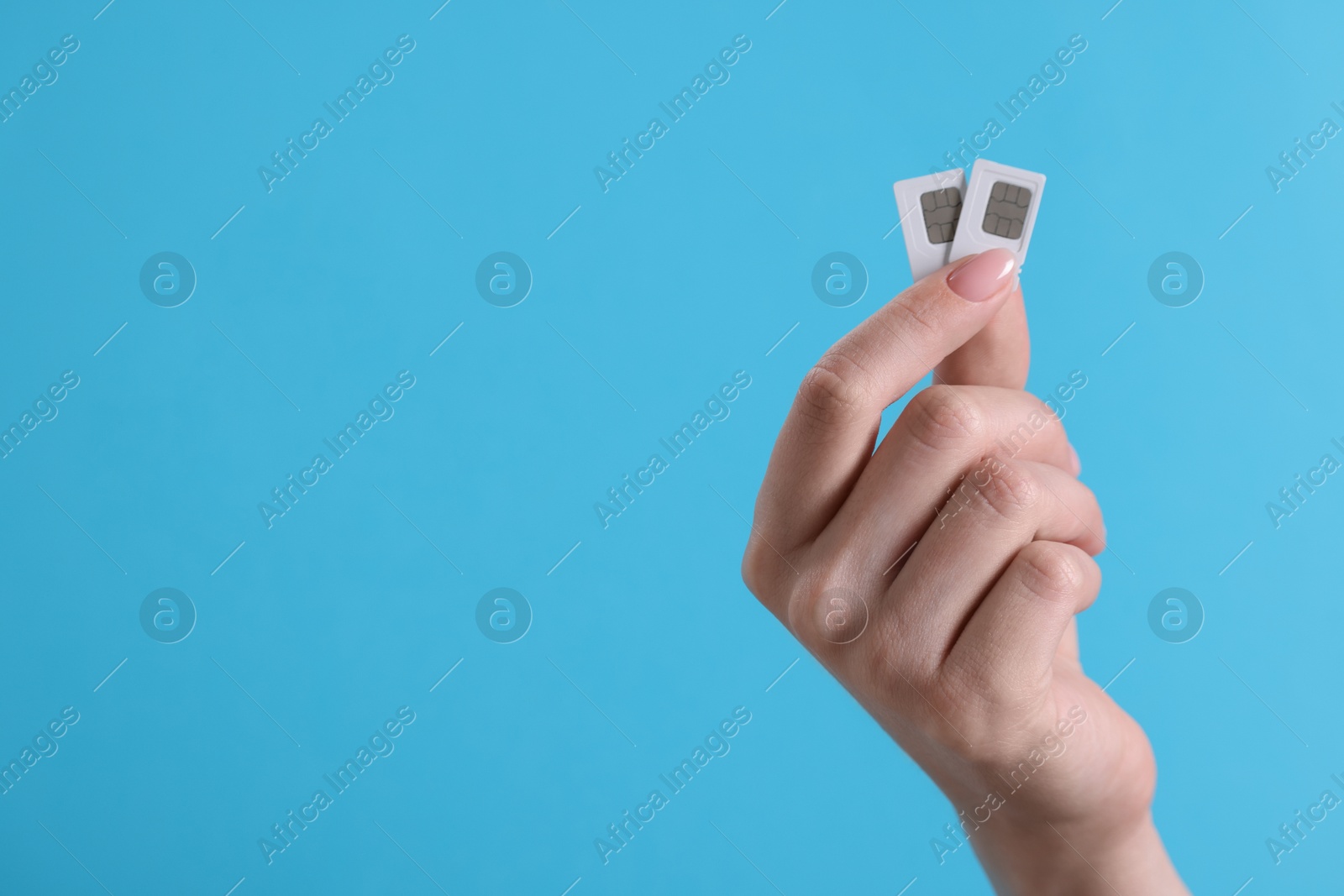 Photo of Woman holding SIM cards on light blue background, closeup. Space for text