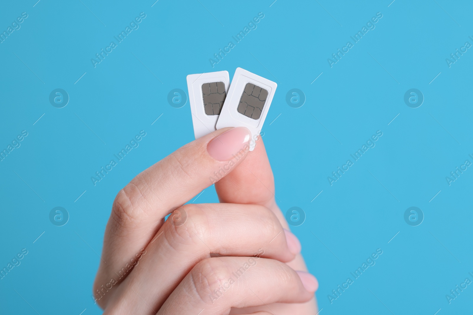 Photo of Woman holding SIM cards on light blue background, closeup