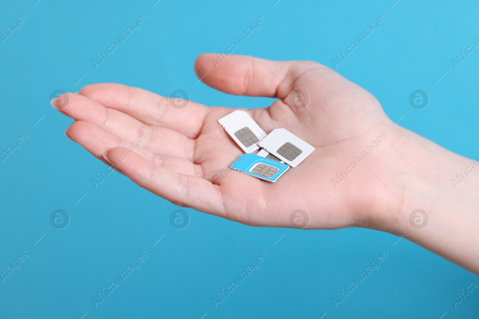 Photo of Woman holding SIM cards on light blue background, closeup