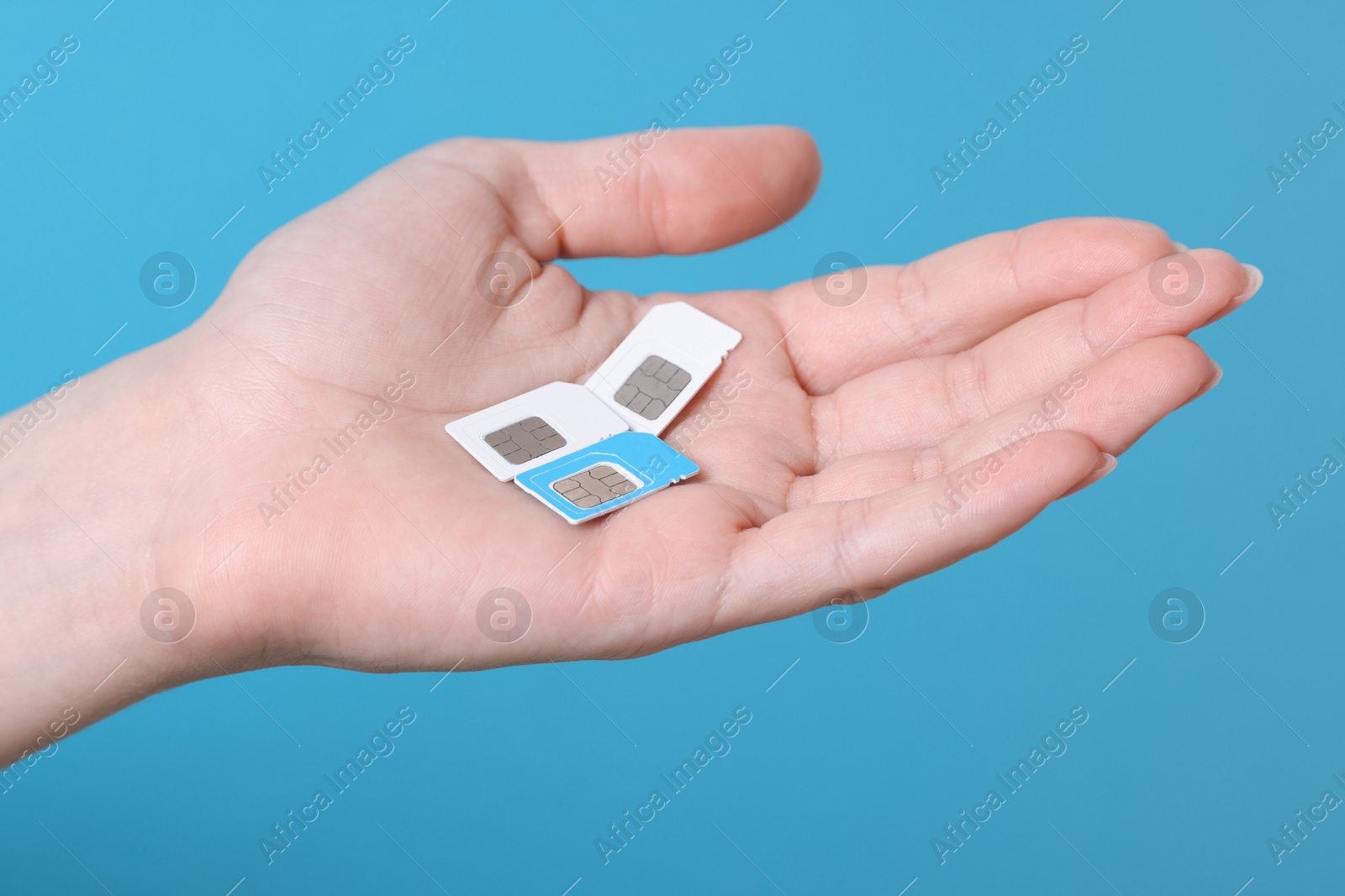 Photo of Woman holding SIM cards on light blue background, closeup