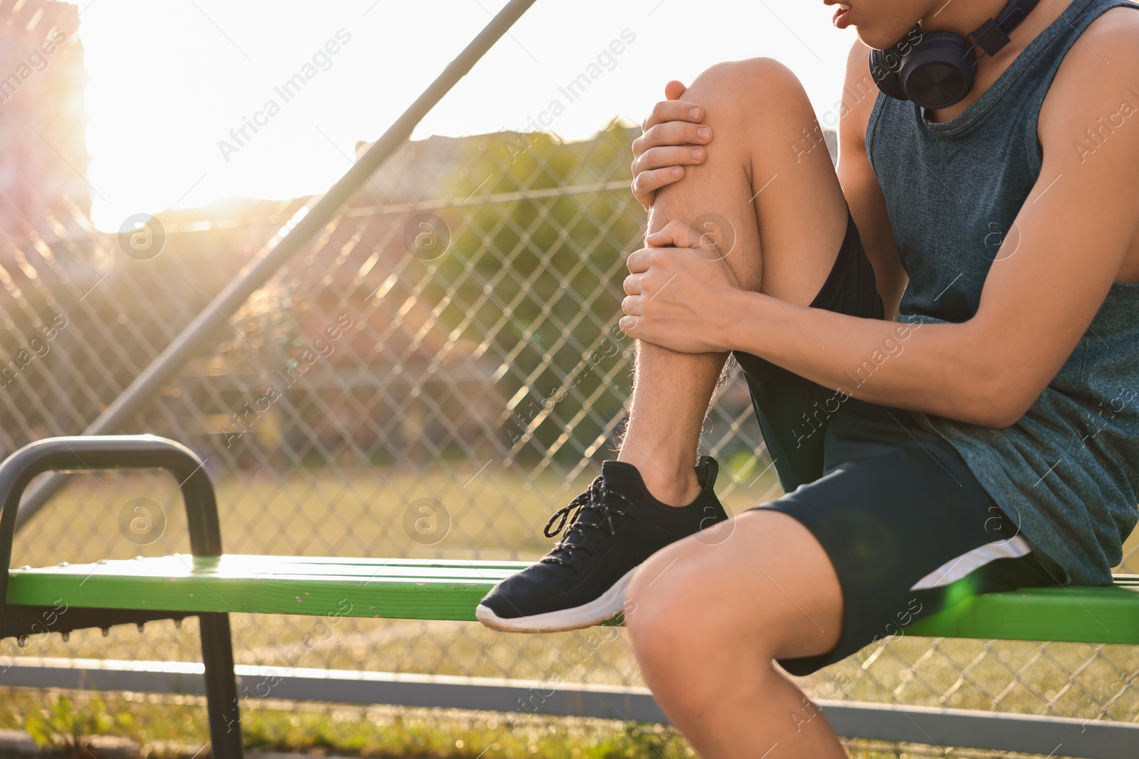 Photo of Sportsman with leg injury suffering from knee pain on bench at stadium, closeup. Space for text