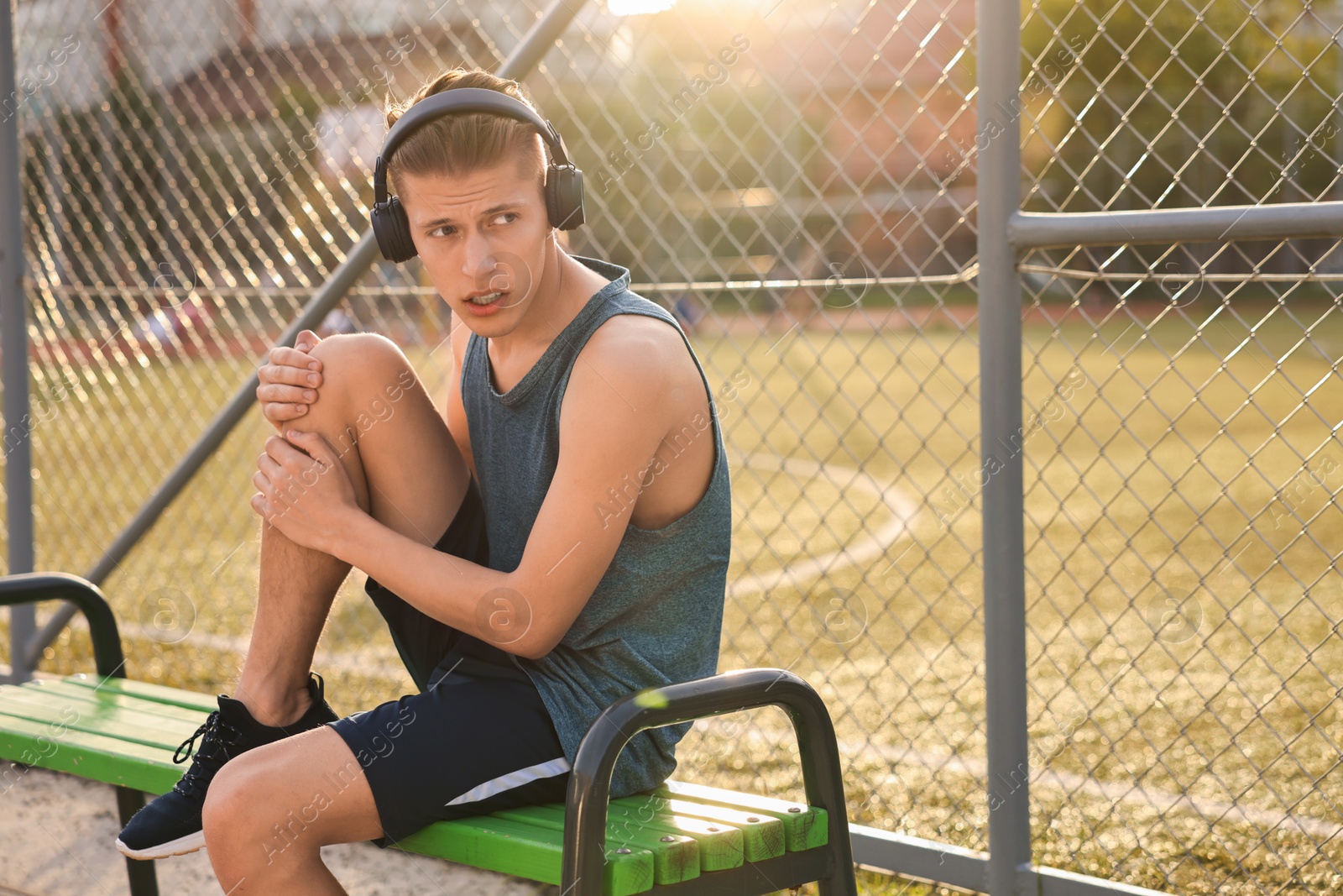 Photo of Sportsman with leg injury suffering from knee pain on bench at stadium, space for text