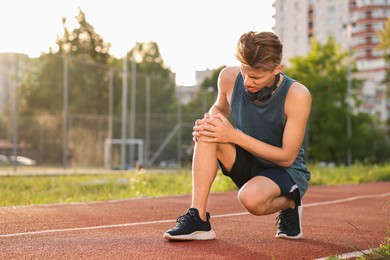 Sportsman with leg injury suffering from knee pain at stadium, space for text