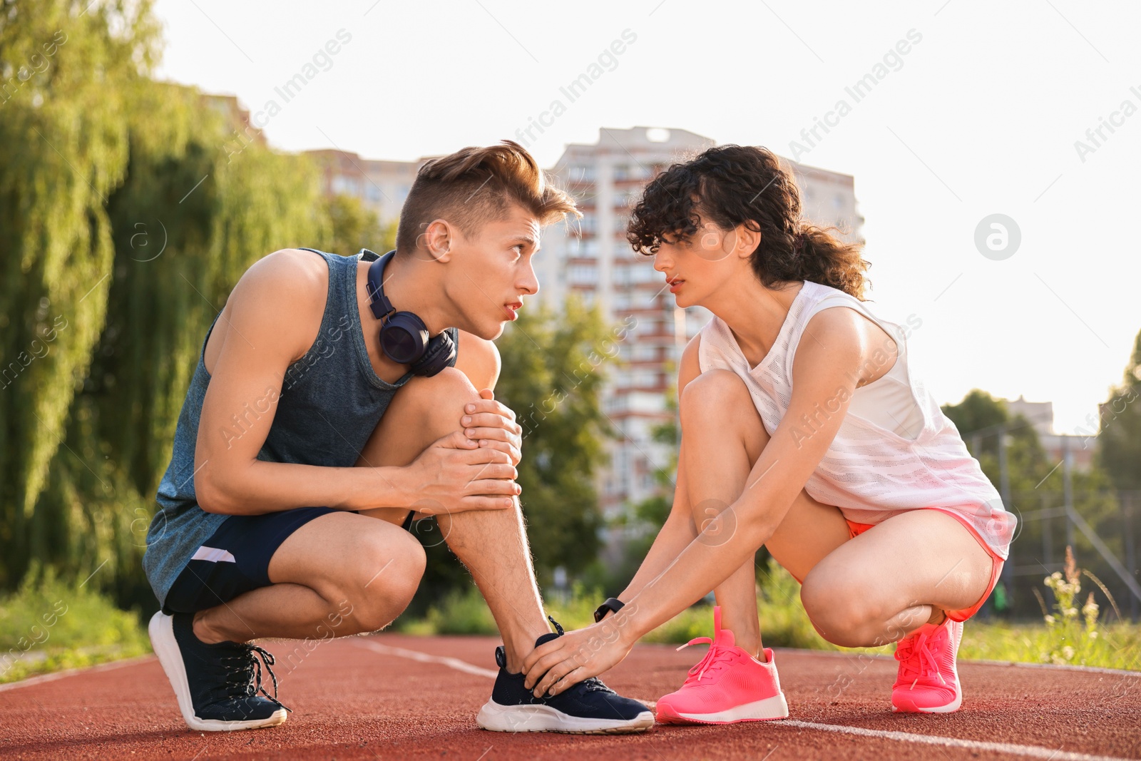 Photo of Sports injury. Woman helping man with leg pain at stadium