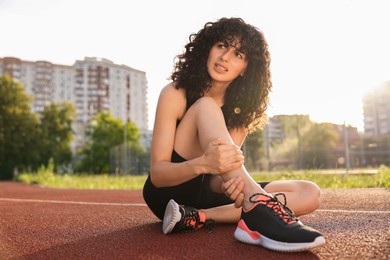 Sports injury. Woman suffering from leg pain at stadium