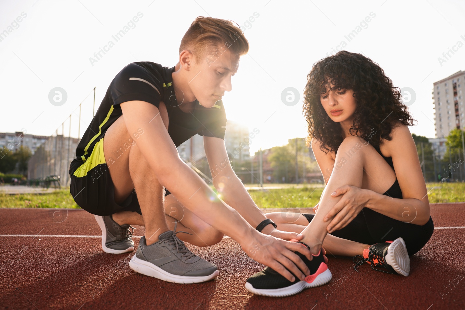 Photo of Sports injury. Man helping woman with leg pain at stadium