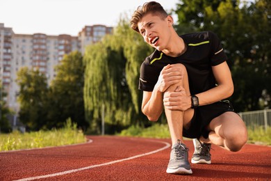 Sportsman with leg injury suffering from knee pain at stadium, space for text