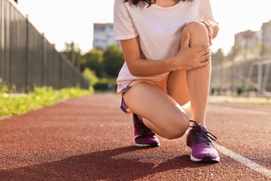 Photo of Sportswoman with leg injury suffering from knee pain at stadium, closeup. Space for text