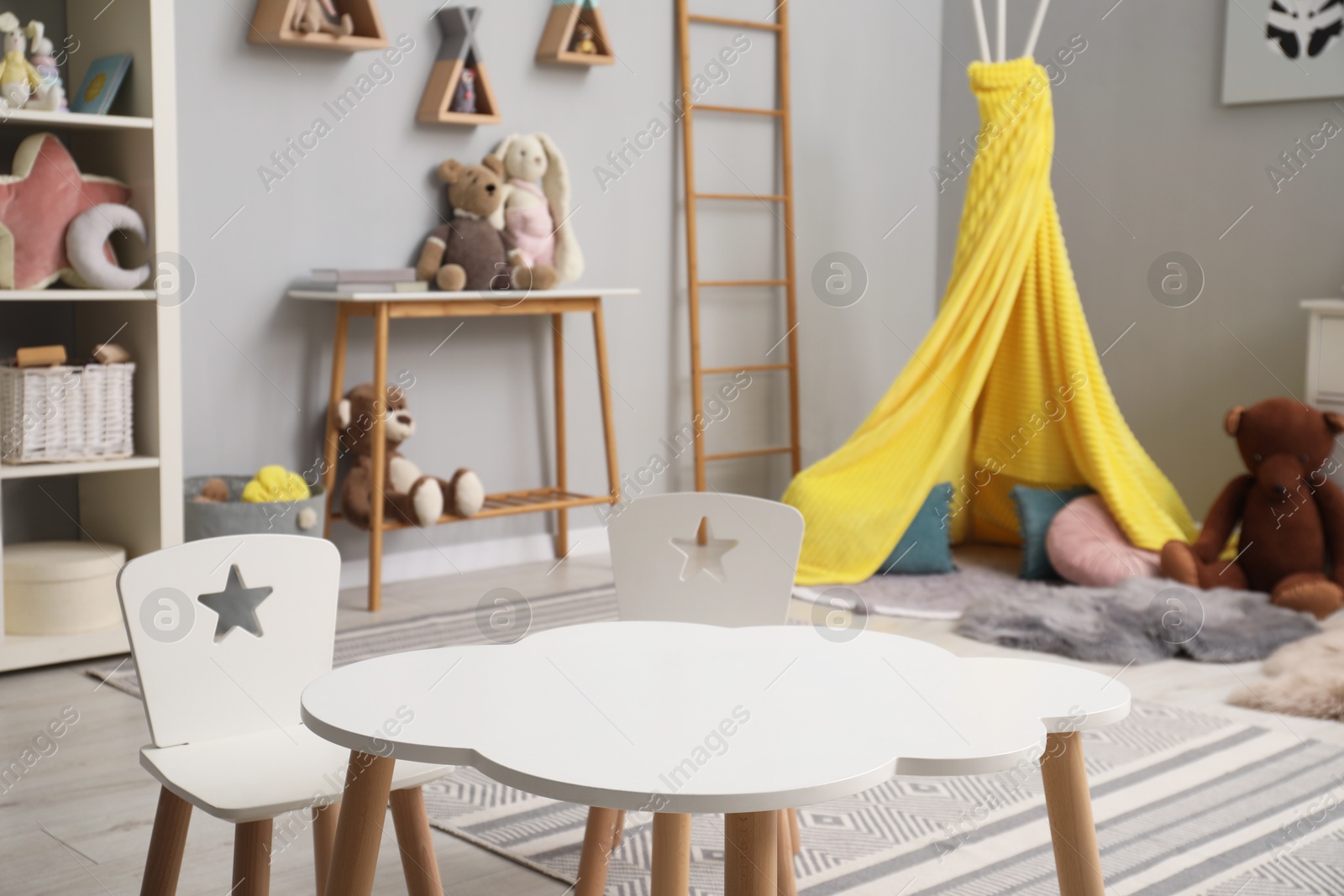 Photo of Stylish child room interior with table, chairs, toys and play tent