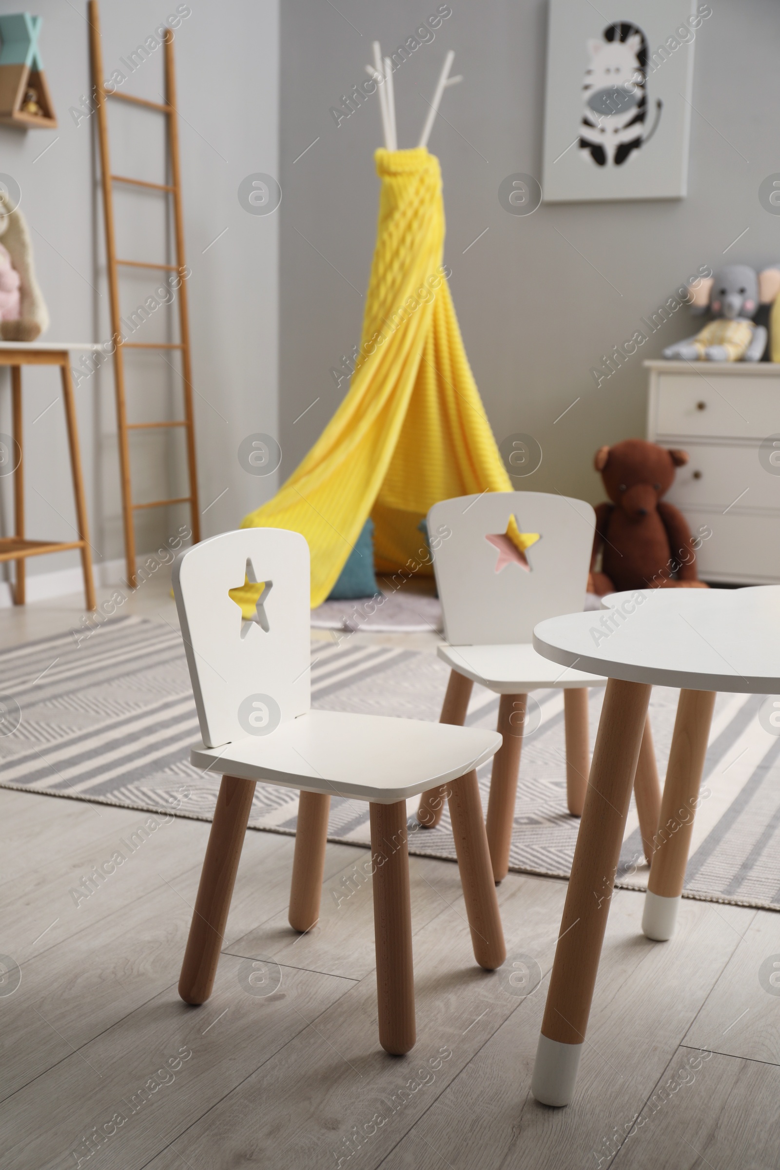 Photo of Stylish child room interior with table, chairs, toys and play tent