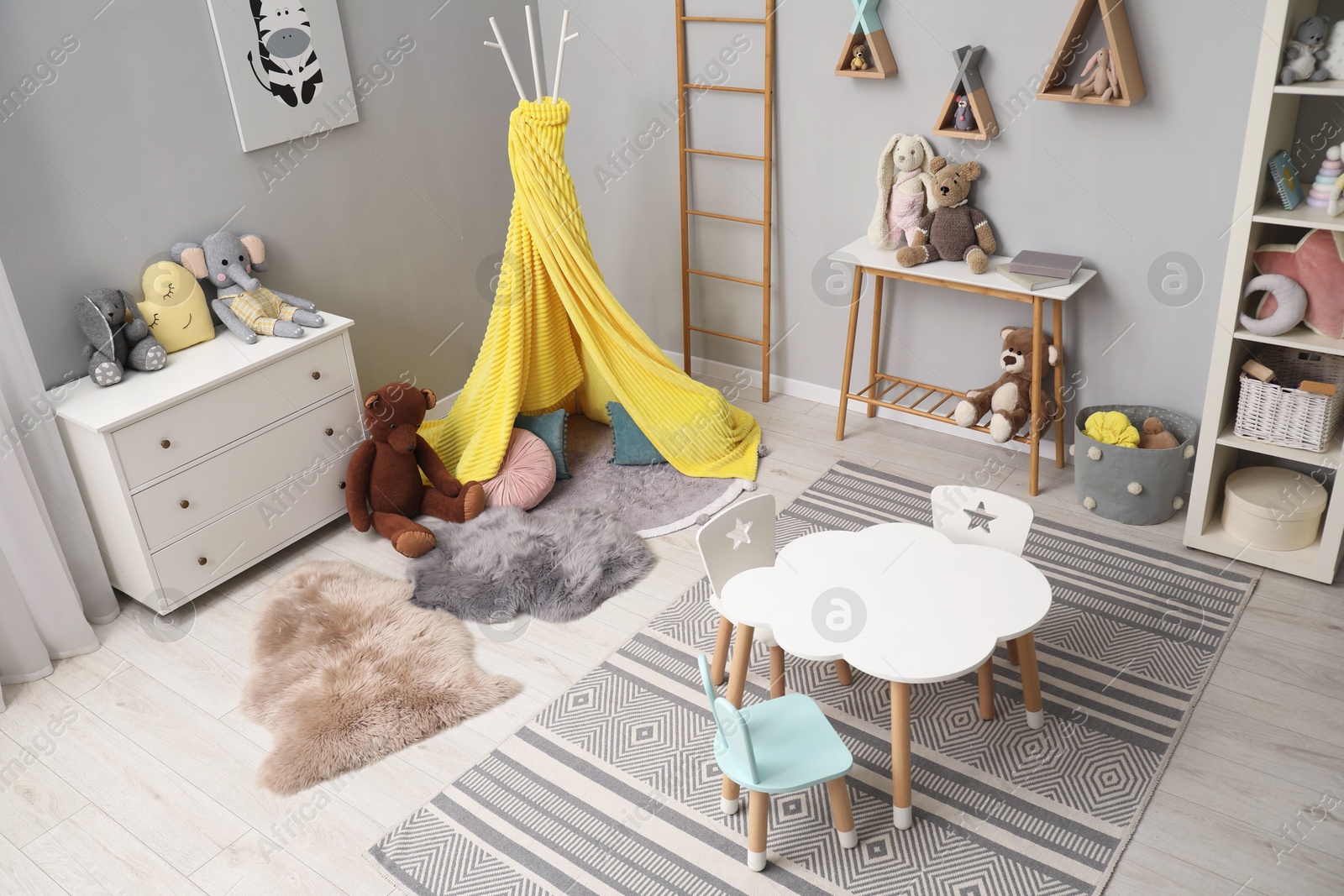 Photo of Stylish child room interior with table, chairs, toys and play tent