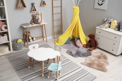 Photo of Stylish child room interior with table, chairs, toys and play tent