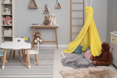 Photo of Stylish child room interior with table, chairs, toys and play tent