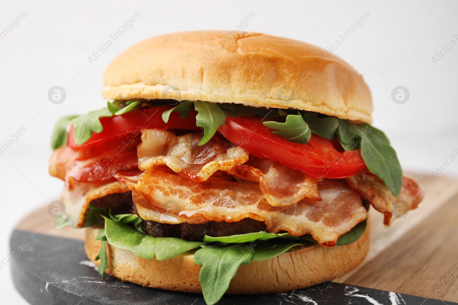 Photo of Delicious burger with bacon, tomato and greens on light background, closeup