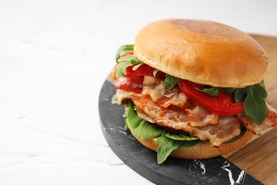 Photo of Delicious burger with bacon, tomato and greens on light textured table, closeup. Space for text