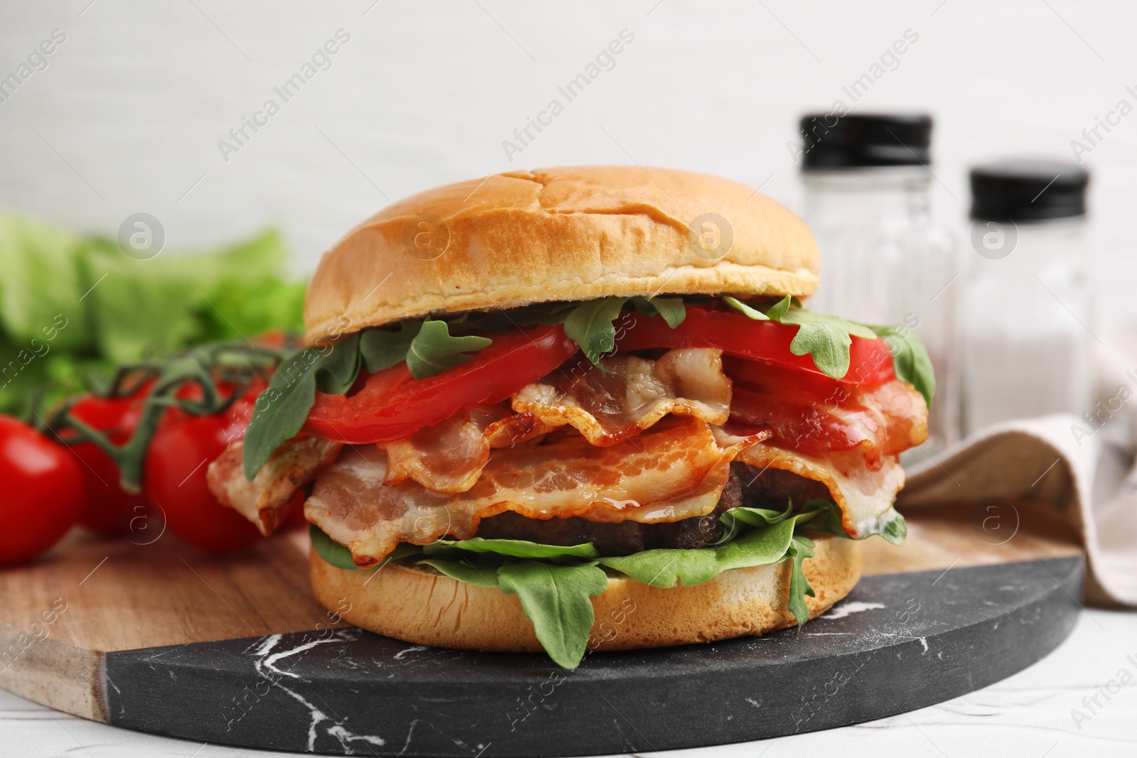 Photo of Delicious burger with bacon, tomato and greens on light table, closeup