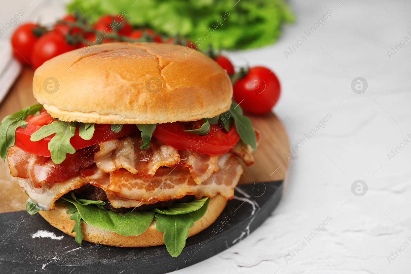 Photo of Delicious burger with bacon, tomato and greens on light textured table, closeup. Space for text