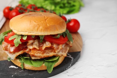 Delicious burger with bacon, tomato and greens on light textured table, closeup. Space for text