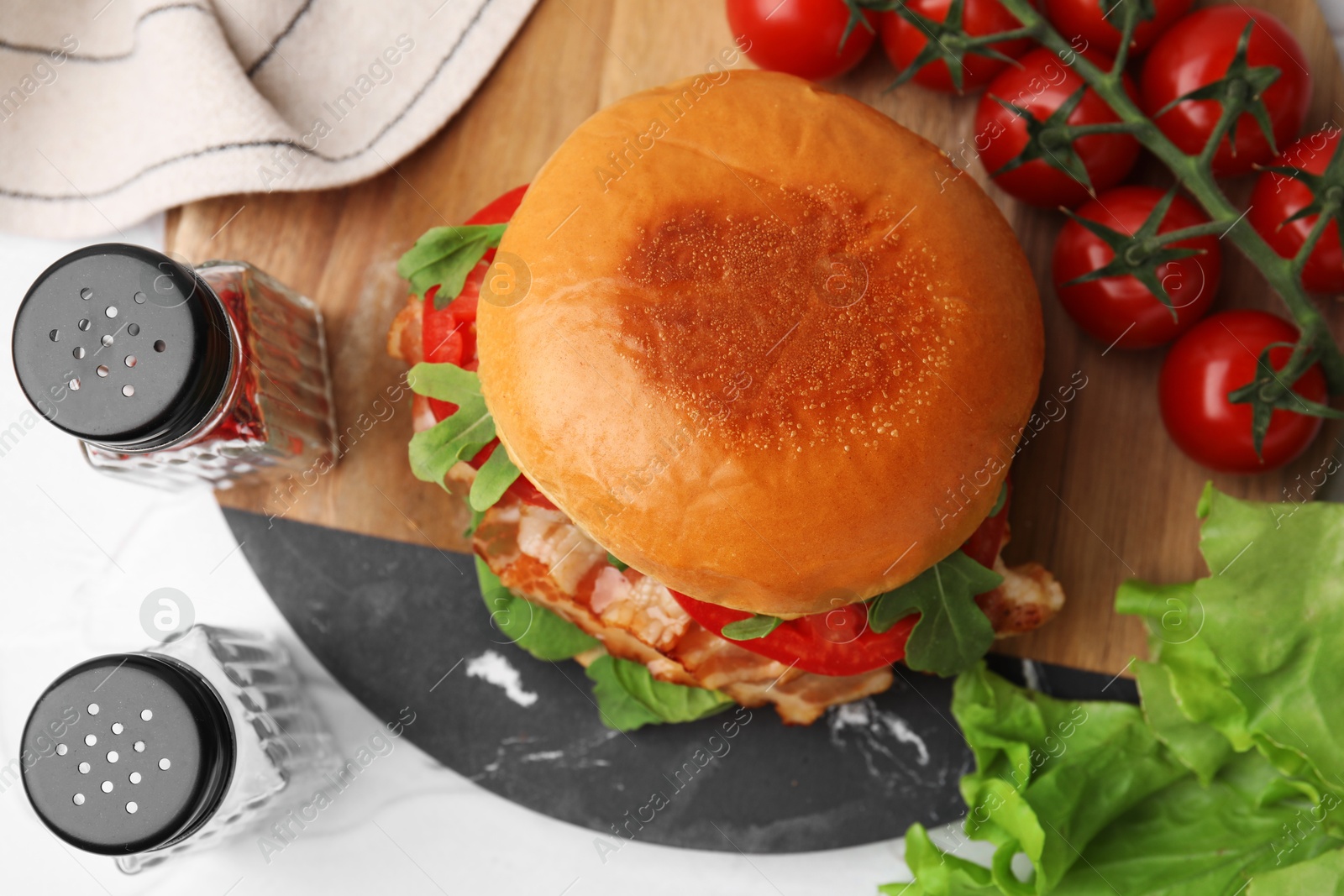 Photo of Delicious burger with bacon, tomatoes and lettuce on light table, flat lay