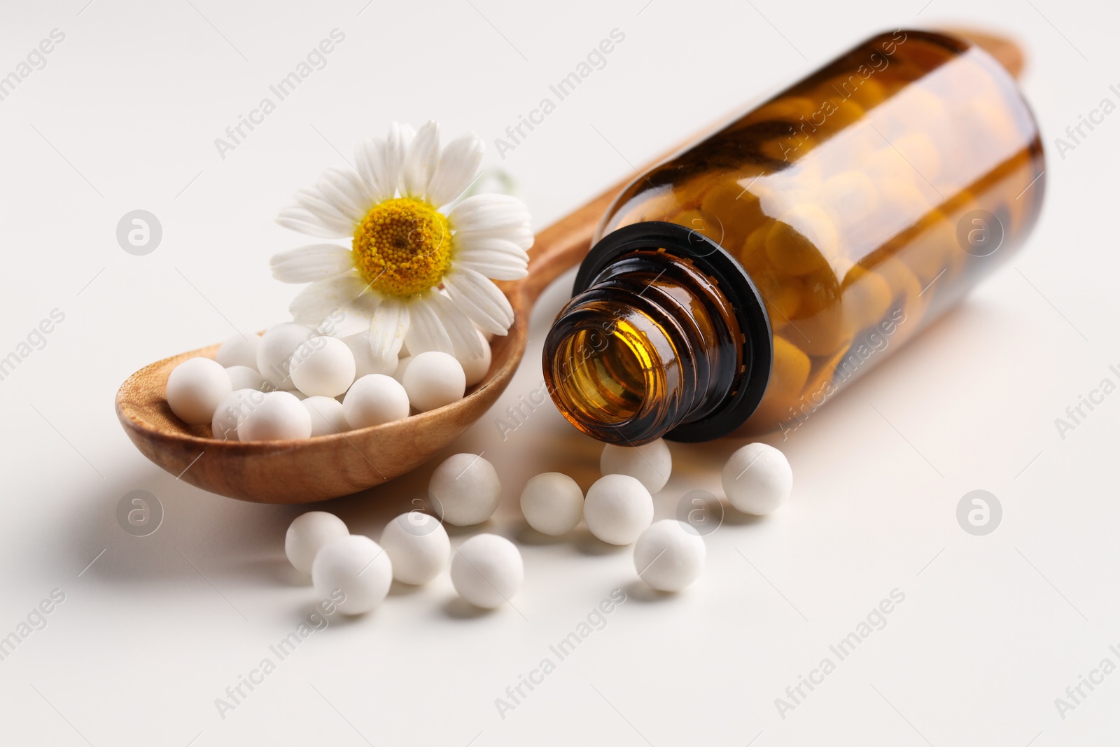 Photo of Homeopathic remedy. Spoon with pills, bottle and chamomile flower on white background