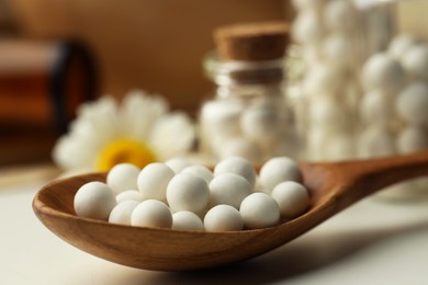 Photo of Homeopathic remedy. Spoon with pills and chamomile flowers on white table, closeup