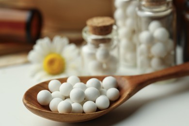 Photo of Homeopathic remedy. Spoon with pills, bottles and chamomile flowers on white table, closeup