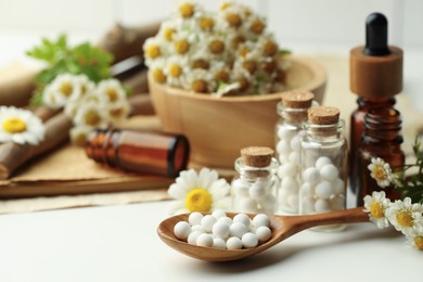 Photo of Homeopathic remedy. Spoon with pills, bottles and chamomile flowers on white table, closeup