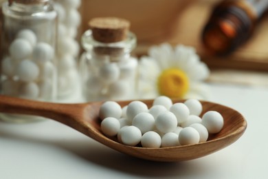 Photo of Homeopathic remedy. Spoon with pills, bottles and chamomile flowers on white table, closeup