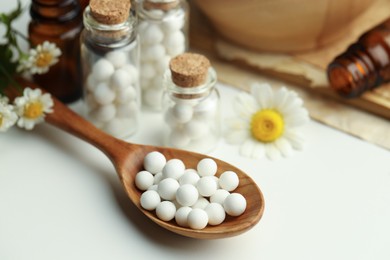 Homeopathic remedy. Spoon with pills, bottles and chamomile flowers on white table, closeup