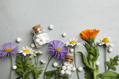 Homeopathic remedy. Different flowers, pills and glass bottles on grey table, flat lay