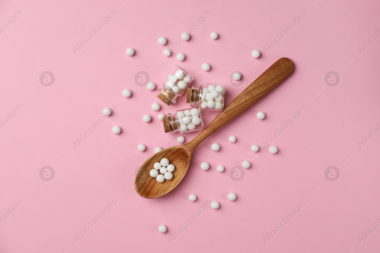 Photo of Homeopathic remedy. Glass bottles, pills and wooden spoon on pink background, flat lay