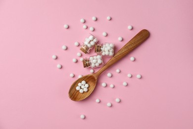 Homeopathic remedy. Glass bottles, pills and wooden spoon on pink background, flat lay