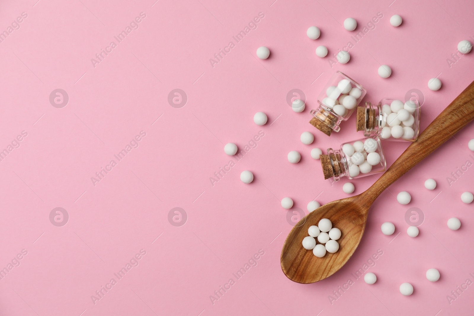 Photo of Homeopathic remedy. Glass bottles, pills and wooden spoon on pink background, flat lay. Space for text