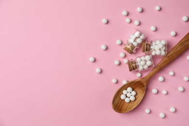 Photo of Homeopathic remedy. Glass bottles, pills and wooden spoon on pink background, flat lay. Space for text